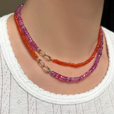 A woman in a plain white t-shirt shows wears two AMANDA PEARL necklaces. A fuchsia faceted sapphire necklace and a carnelian faceted necklace. She shows off the dramatic evolution clasp.