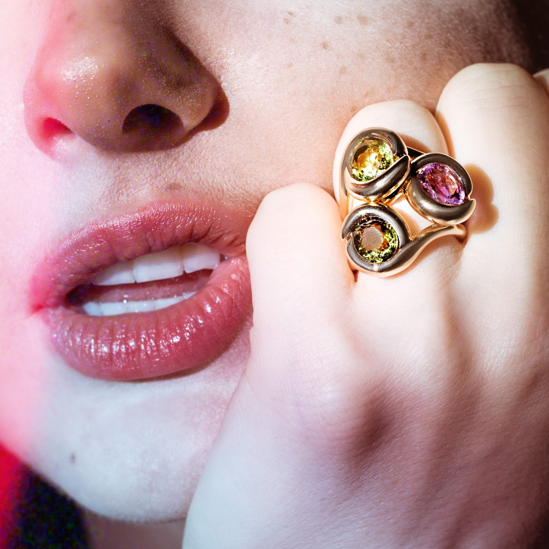 A close up of a model wearing an AMANDA PEARL recycled 14K amethyst and two green tourmaline molten knot rings on one finger. 