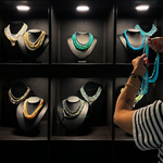 Amanda Brotman's hands are shown holding a strand of blue opal beaded necklace strands, organizing them on black mannequin busts at the AMANDA PEARL showroom in NYC.