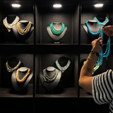 Amanda Brotman's hands are shown holding a strand of blue opal beaded necklace strands, organizing them on black mannequin busts at the AMANDA PEARL showroom in NYC.
