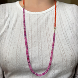 A woman in a plain white t-shirt shows how you can use your AMANDA PEARL evolution clasp to attach a fuchsia sapphire necklace to a carnelian faceted necklace to make one long, two tone necklace.
