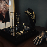 A styled jewelry display at the AMANDA PEARL showroom, with a  necklace stand wearing layered gold necklaces, rings, bracelets and necklaces styles neatly against a dark wall.