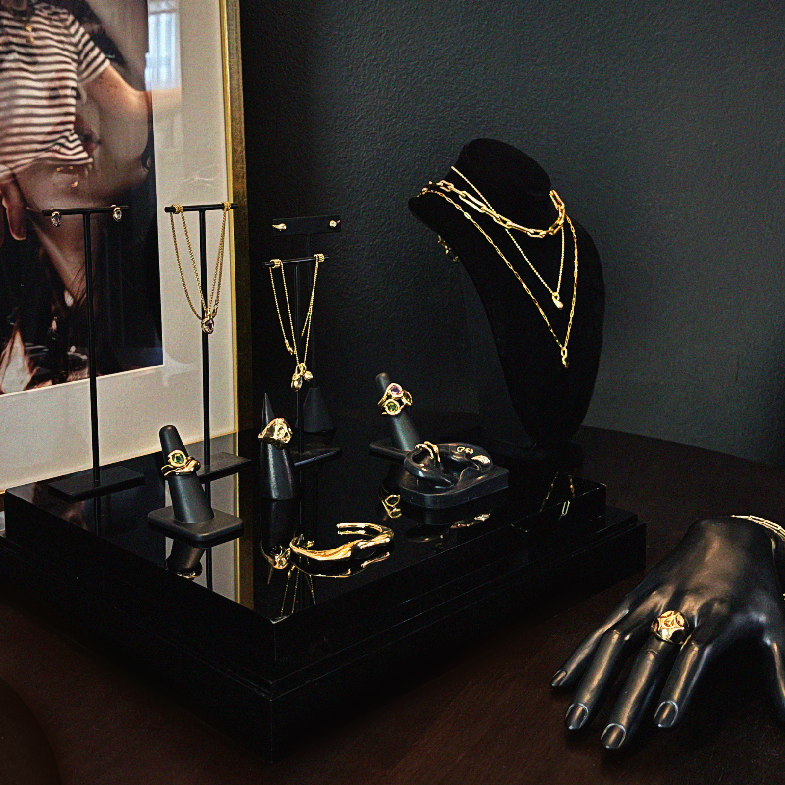 A styled jewelry display at the AMANDA PEARL showroom, with a  necklace stand wearing layered gold necklaces, rings, bracelets and necklaces styles neatly against a dark wall.