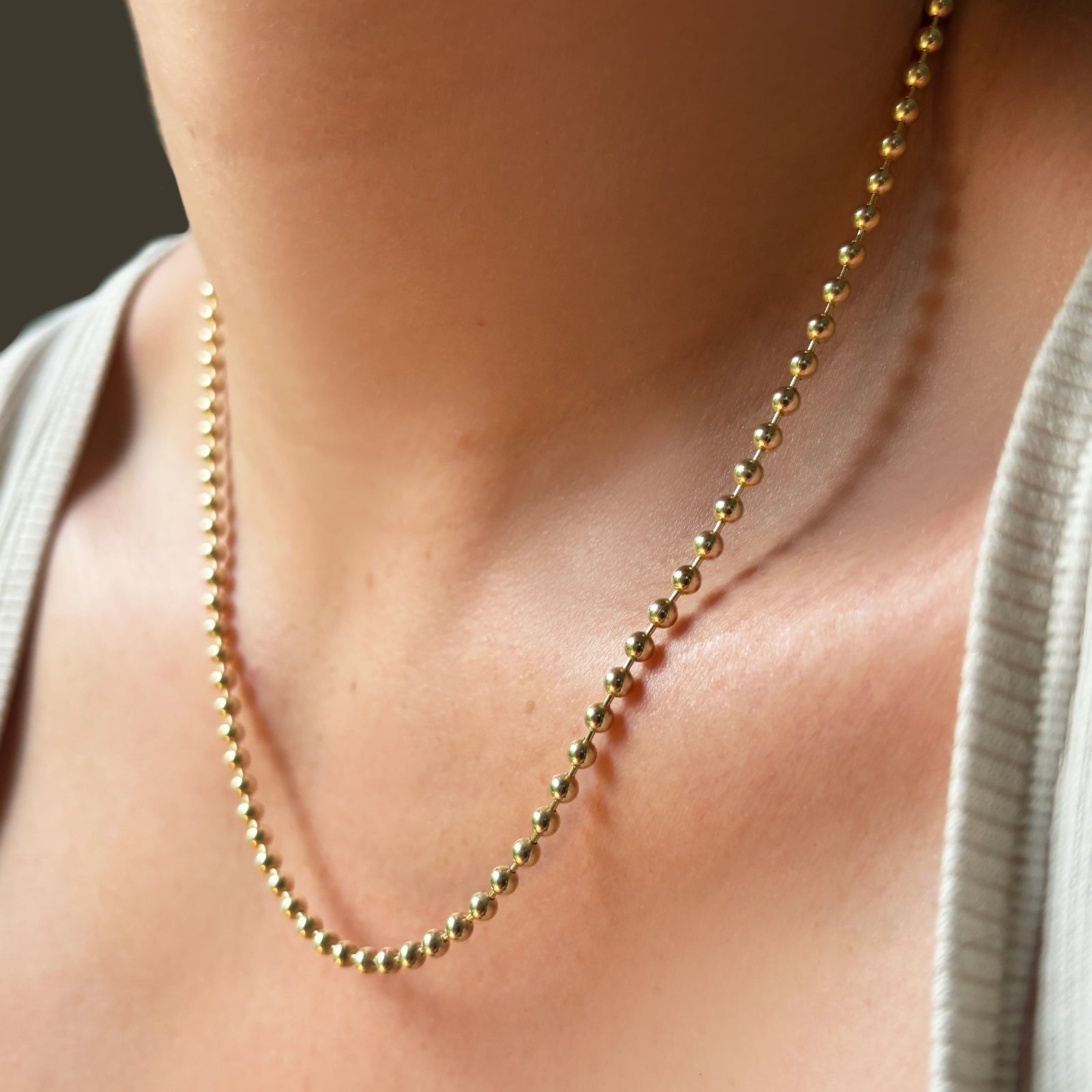 3mm bead chain necklace in yellow gold on the neck at an angle.