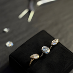 Three AMANDA PEARL rings in 14K recycled yellow and white gold, with lab grown diamonds, sit on a ring cushion with a pair of pliers and l,oose diamonds behind them.