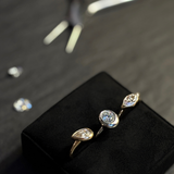 Three AMANDA PEARL rings in 14K recycled yellow and white gold, with lab grown diamonds, sit on a ring cushion with a pair of pliers and l,oose diamonds behind them.