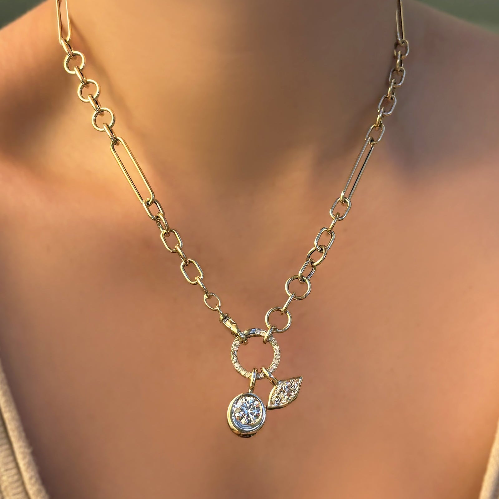 Chunky irregular cable chain with round pavé face charm lock dropping two molten solitaire charms on a model's neck.