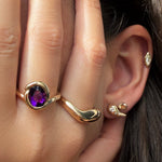 Recycled 14k gold knot ring with deep purple amethyst worn on a model's hand with a gold molten ring, next to an ear with the molten studs with diamonds, small molten stud, and molten marquise solitaire stud.