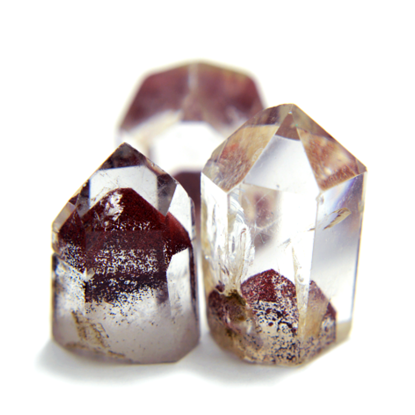 Three phantom clear quartz crystal points with embedded dark reddish-brown and metallic inclusions, photographed on a white background.