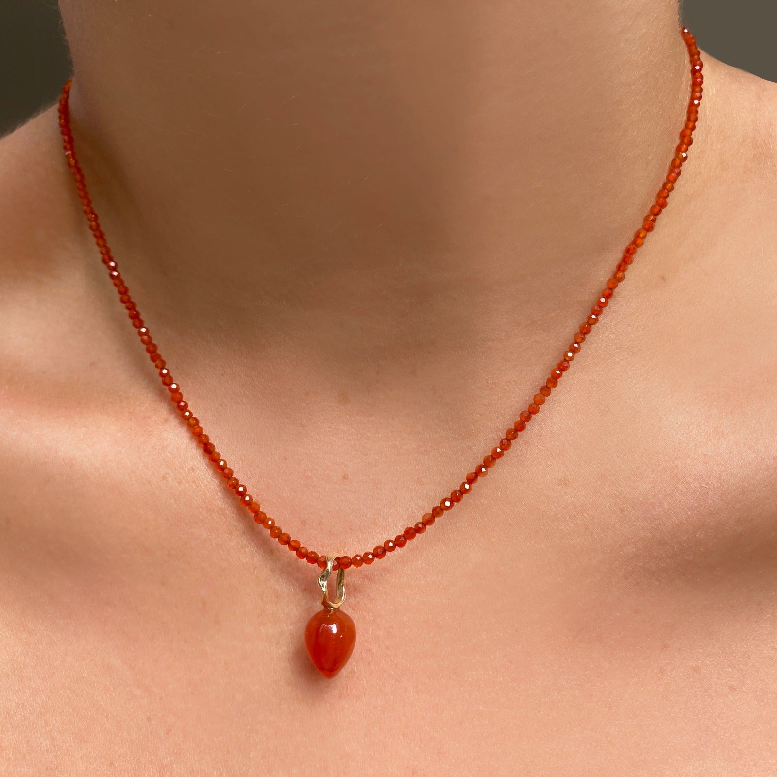 Shimmering slim gemstone beaded necklace made of 2mm faceted stones in carnelian on a gold linking lobster clasp. Styled on a neck with a carnelian acorn drop charm.