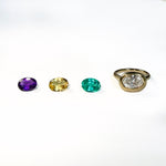 3 colorful oval shaped gemstones next to a yellow gold molten solitaire oval-shaped ring on a white background.