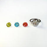 3 colorful faceted round gemstones next to a yellow gold molten solitaire round ring on a white background.