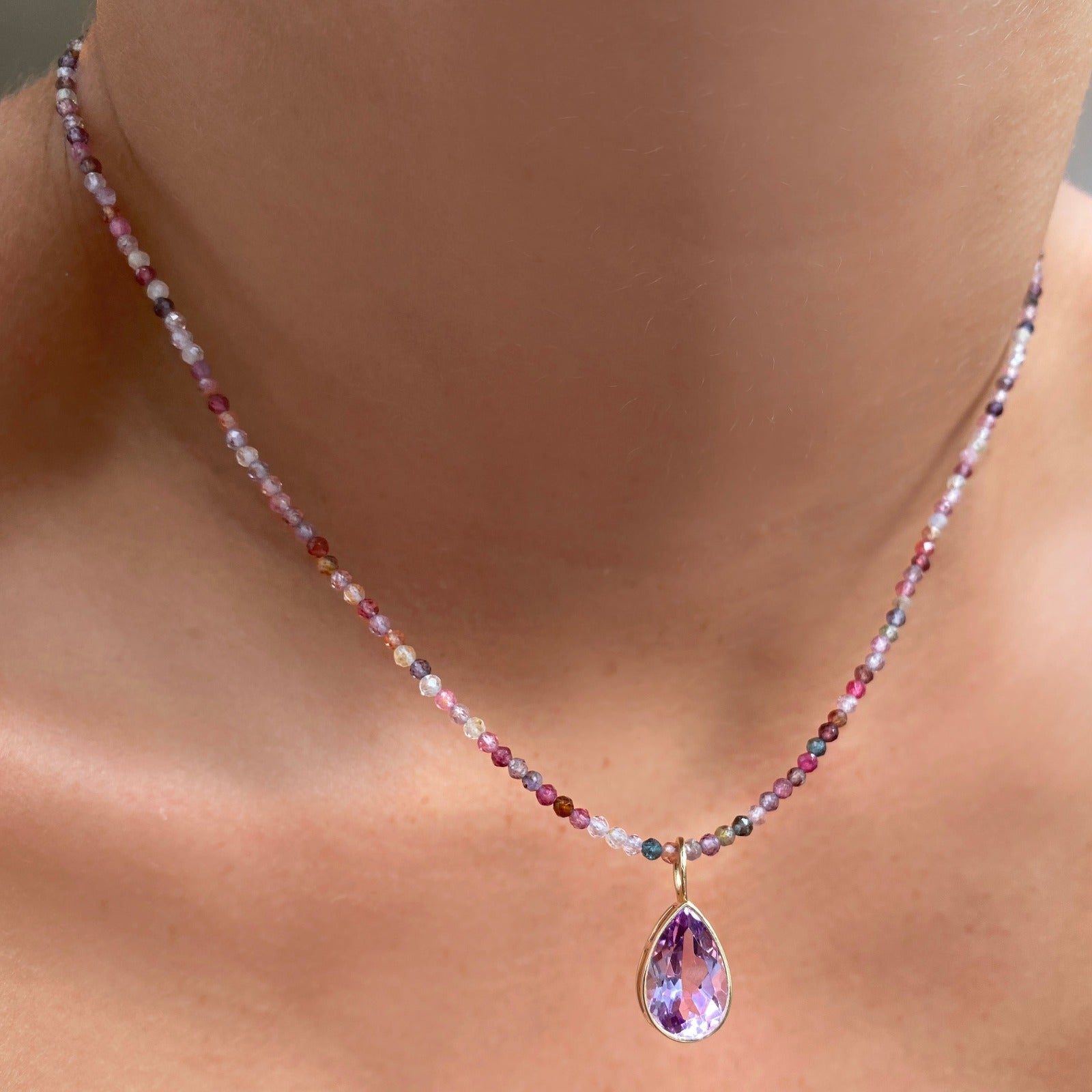Shimmering slim gemstone beaded necklace made of 2mm faceted stones in tourmaline on a gold linking lobster clasp. Styled on a neck layered with pear solitaire charm.
