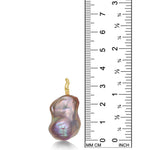 A blush pink baroque pearl pendant from AMANDA PEARL with a recycled 14K yellow gold ripple bale stands next to a ruler for scale.
