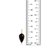 An image of a black agate drop charm, alongside a ruler, showing that the length is 2.5cm. It has a 14k yellow gold ripple shaped bale.
