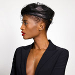 A model in a black beret, with red lipstick, wears a blazer and the quill spike charm in 14K recycled yellow gold, on a chain, hanging alongside the X quill letter charm. She wears the quill climber earrings and small ripple stud earring in her ears. 