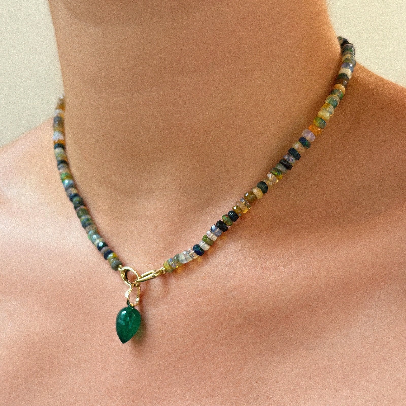 Shimmering beaded necklace made of faceted opals in shades of green, blue, purple, and white on a gold linking ovals clasp styled on a neck styled with an acorn drop charm