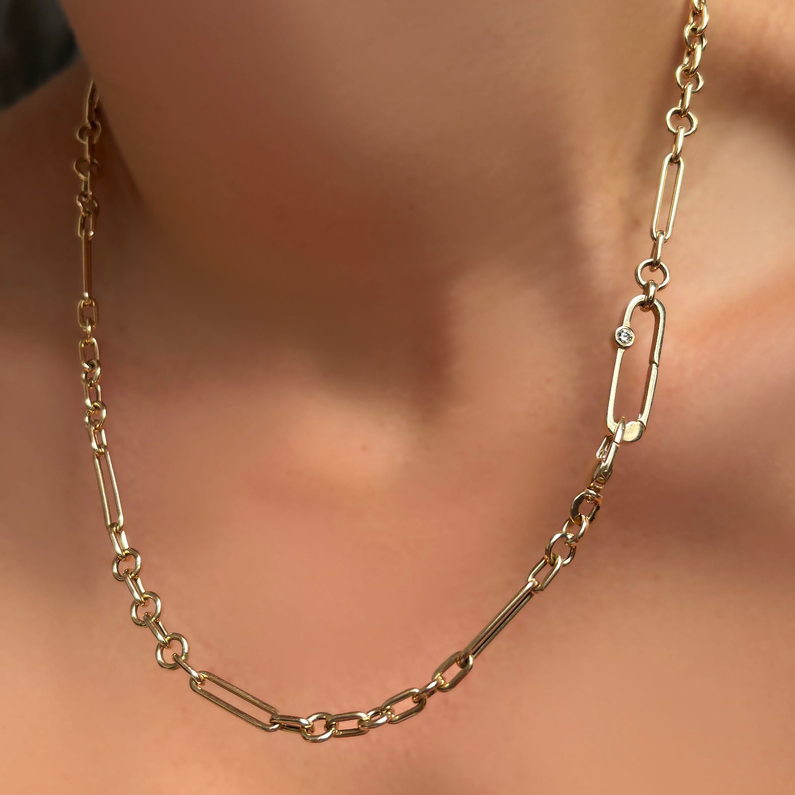 A 6mm Irregular Cable Chain Necklace with paperclip charm lock with diamond on a model's neck both in 14K yellow gold.