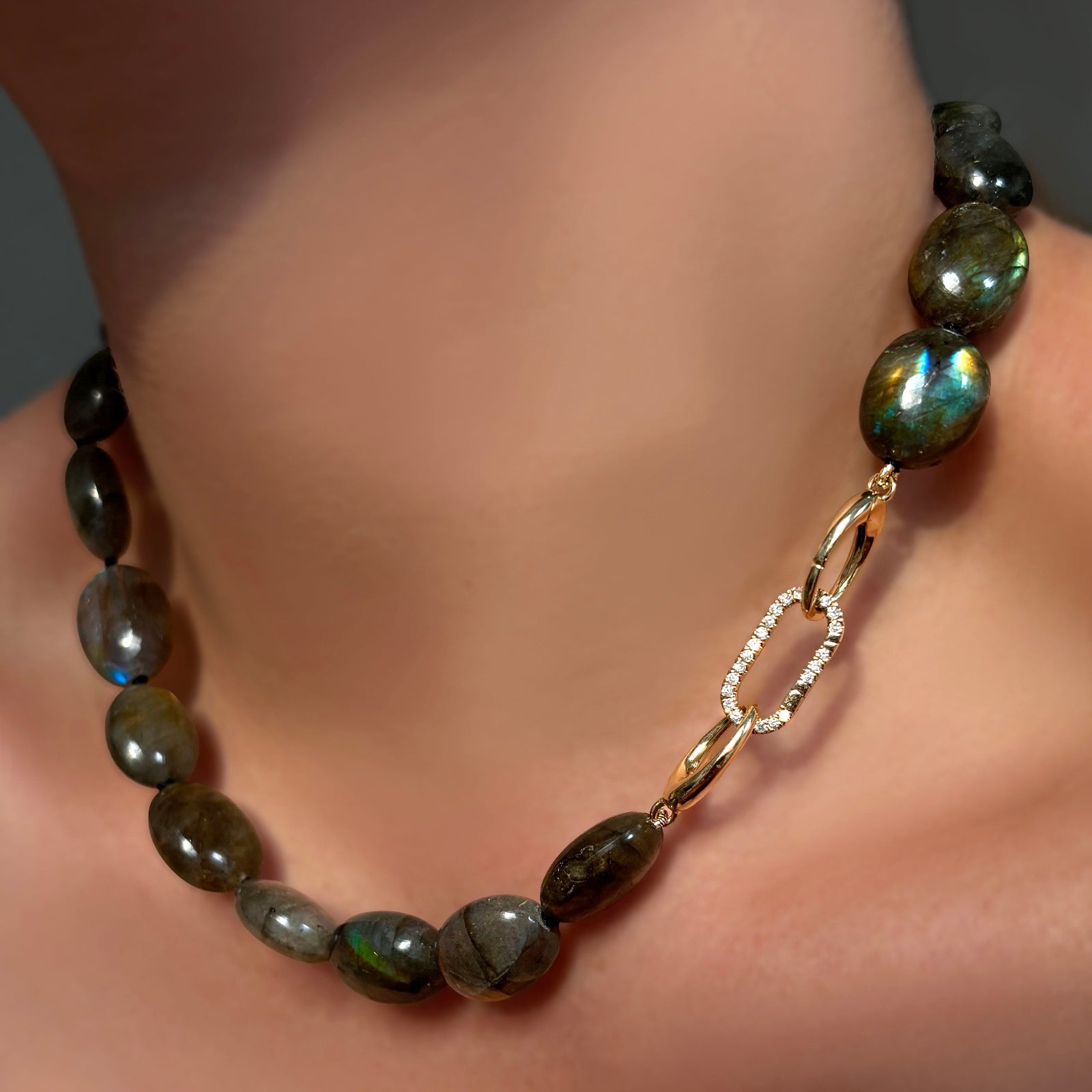 Gemmy and flashy labradorite oval beads with a linking ovals clasp holding a medium pavé face charm lock on a model's neck.