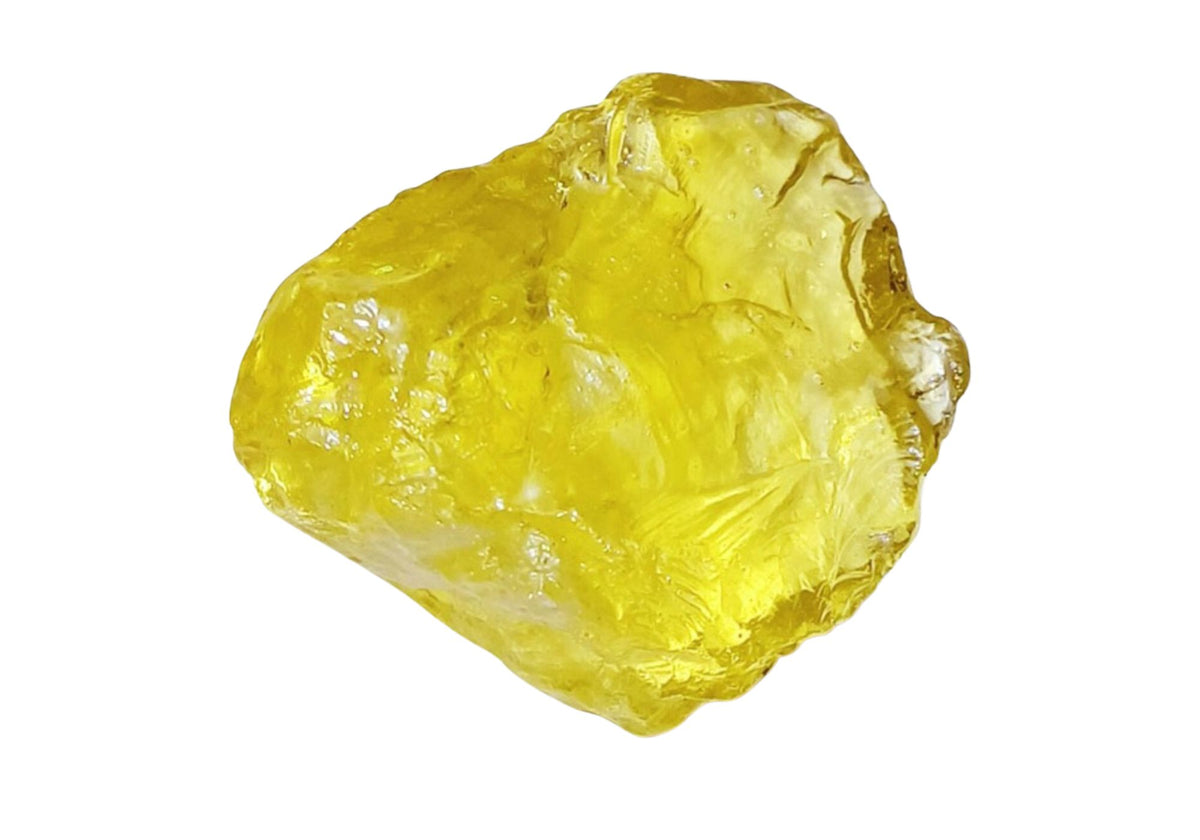 A raw lemon topaz stone sits on a white background.