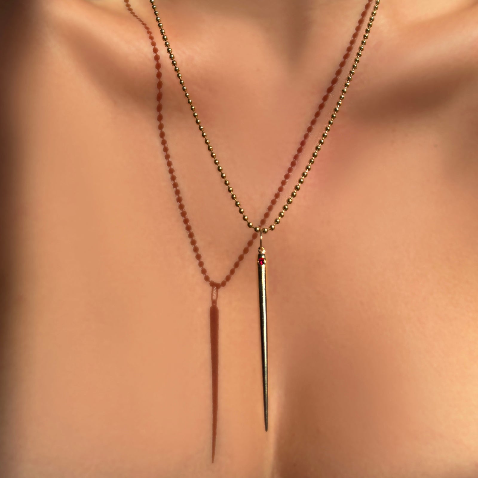 Quill spike charm with ruby gemstone hanging from a 2mm bead chain on a model's neck.
