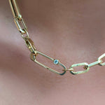 A shiny Paperclip lock charm featuring a 3mm diamond stone clasps an irregular paper clip chain around a model's neck. Both items are cast in 14k yellow gold.