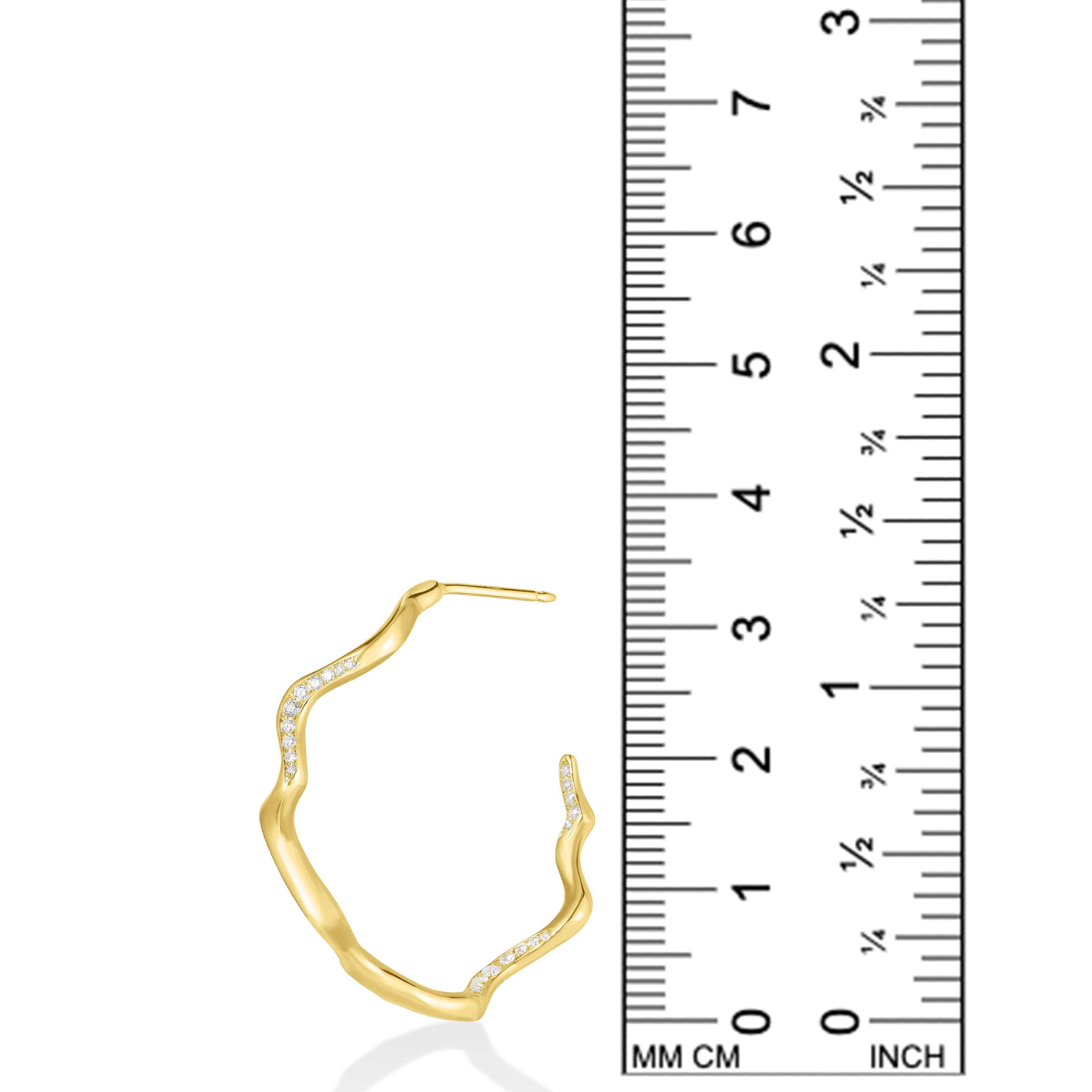 A photo of an undulating hoop earring next to a ruler showing that is is 3.3cm in height. It is made of 14k yellow gold with a rippling shape that is a play on a classic gold hoop earring. It is studded with small diamonds that catch the light and shimmer.