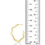 A photo of an undulating hoop earring next to a ruler showing that is is 3.3cm in height. It is made of 14k yellow gold with a rippling shape that is a play on a classic gold hoop earring.