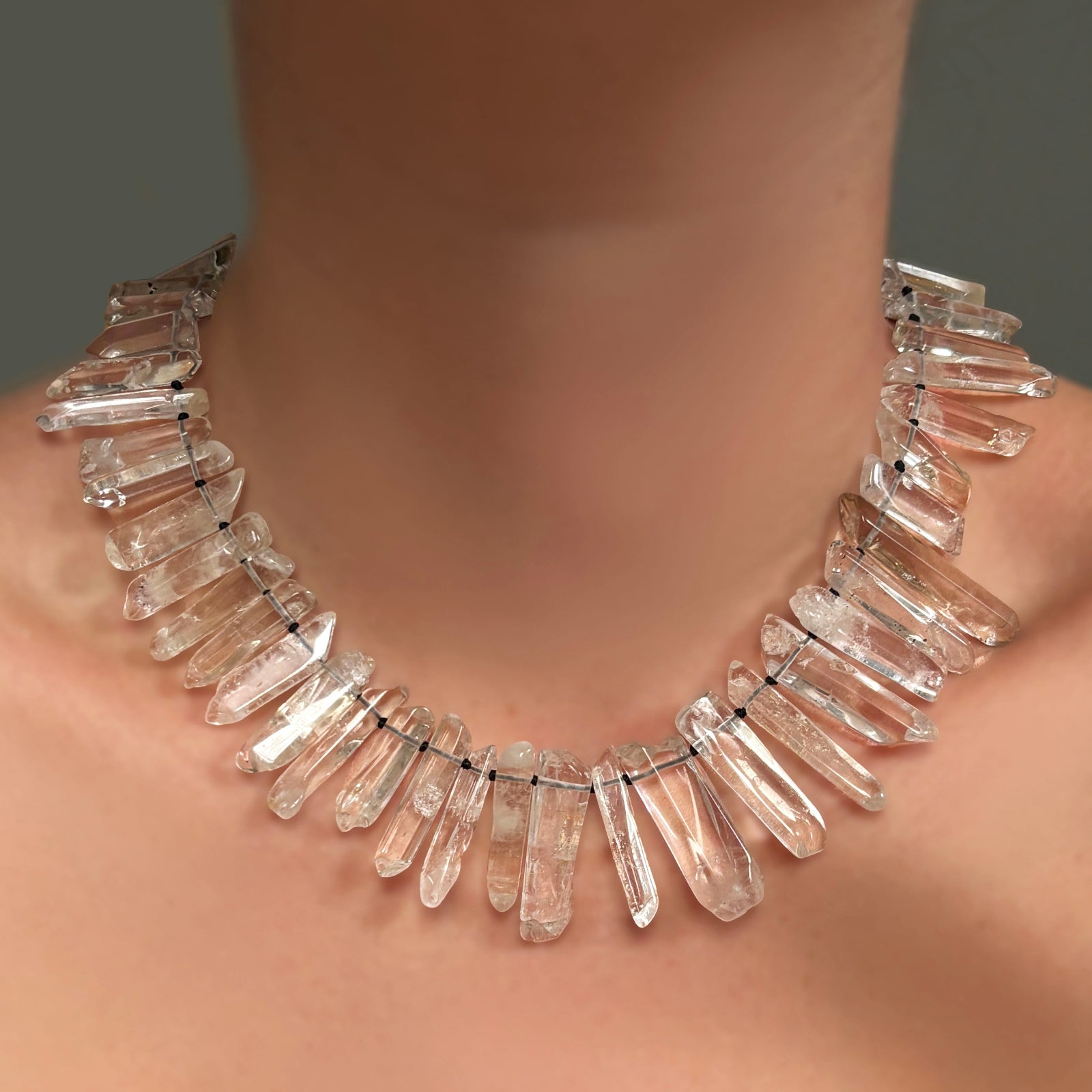 A Rock crystal collar, strung on black thread with knots, on a model's neck.