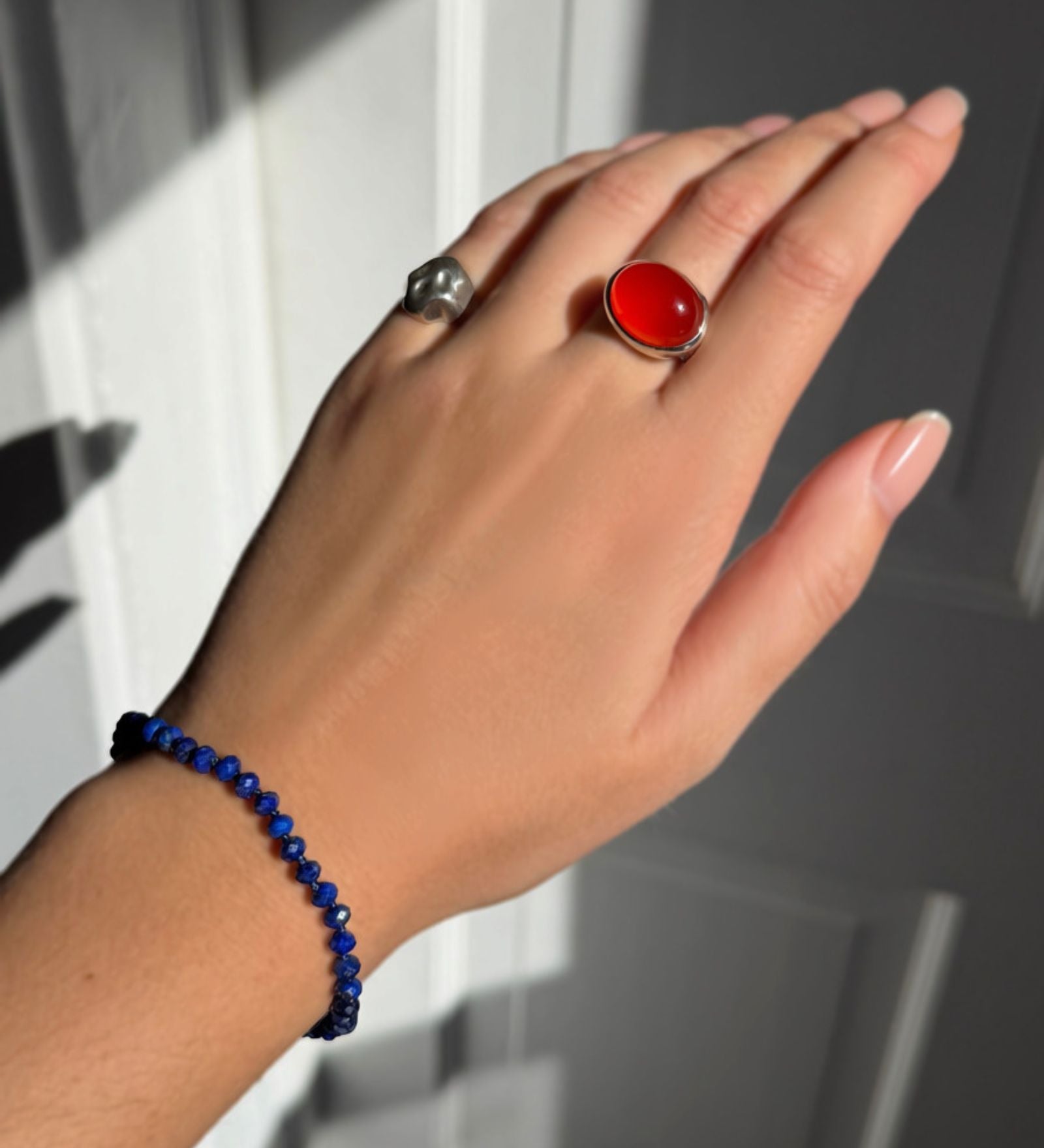 A model wearing an AMANDA PEARL faceted lapis beaded bracelet along with a recycled sterling silver molten skull pinky ring and molten pebble ring with carnelian.