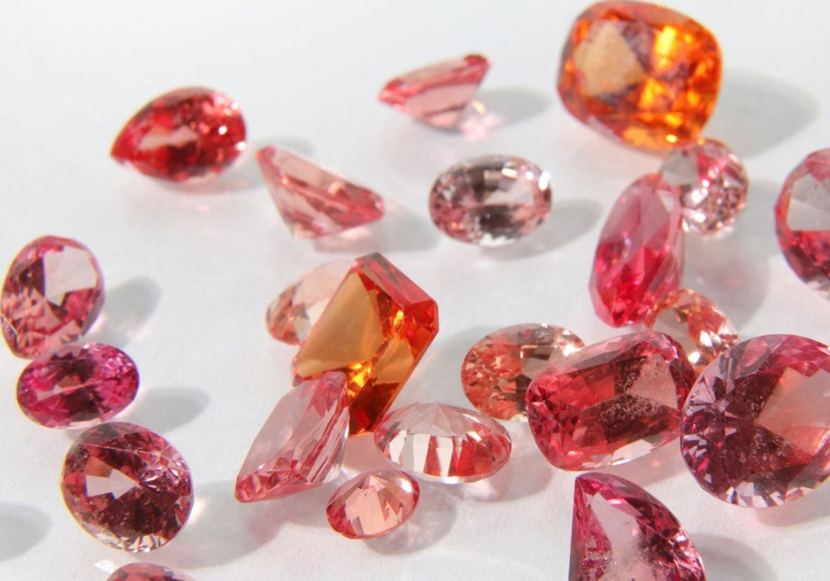 A smattering of pink to orange padparadscha sapphires in different cuts on a white surface. 