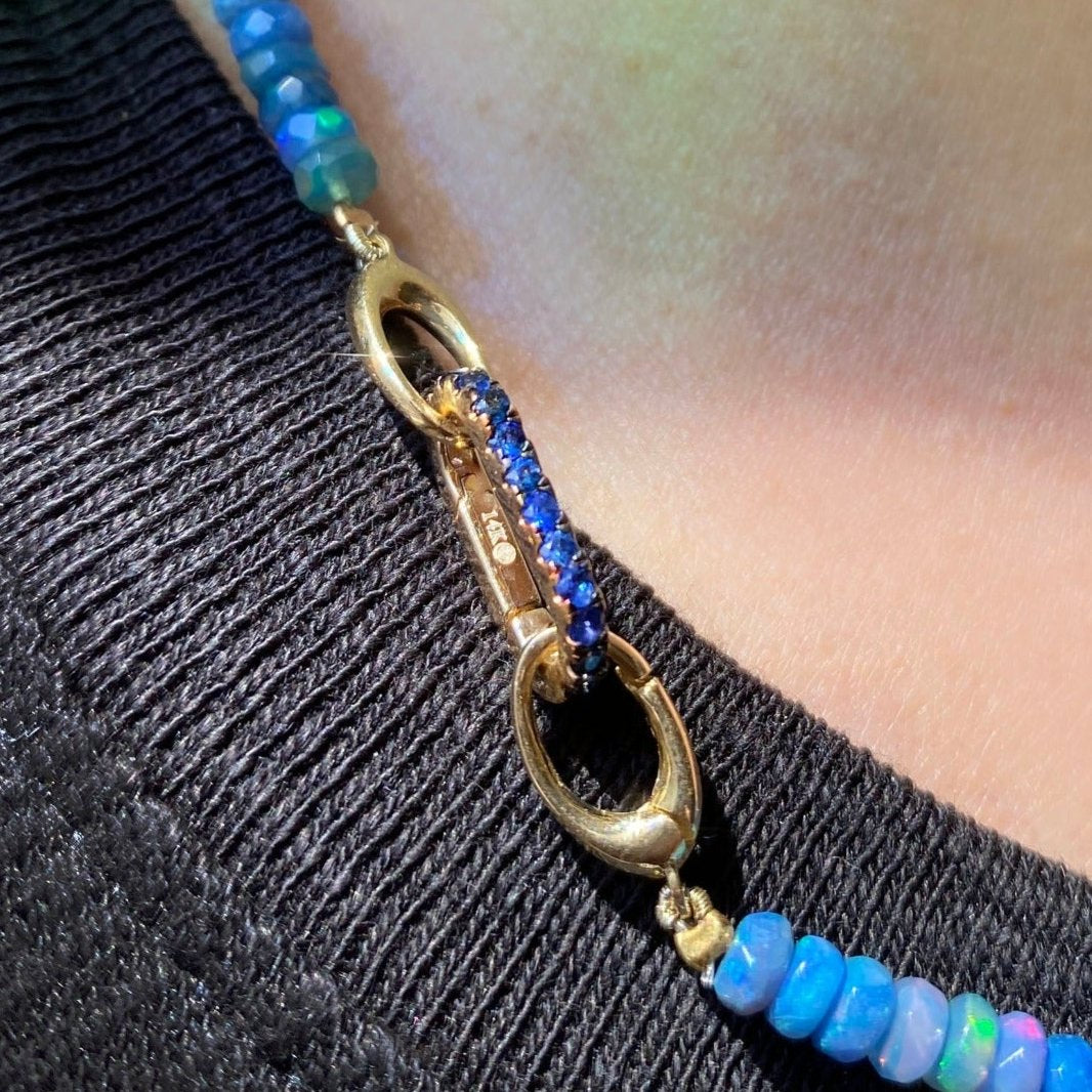 14K gold Small Sapphire Charm Lock styled on a neck locked onto oval clasps of a faceted beaded opal necklace.