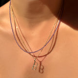 Slim gemstone amethyst layered over a 14k gold diamond cut bead chain with letter "b" charm, hanging on a model's neck.