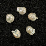 Various organically shaped baroque pearls on black sand.