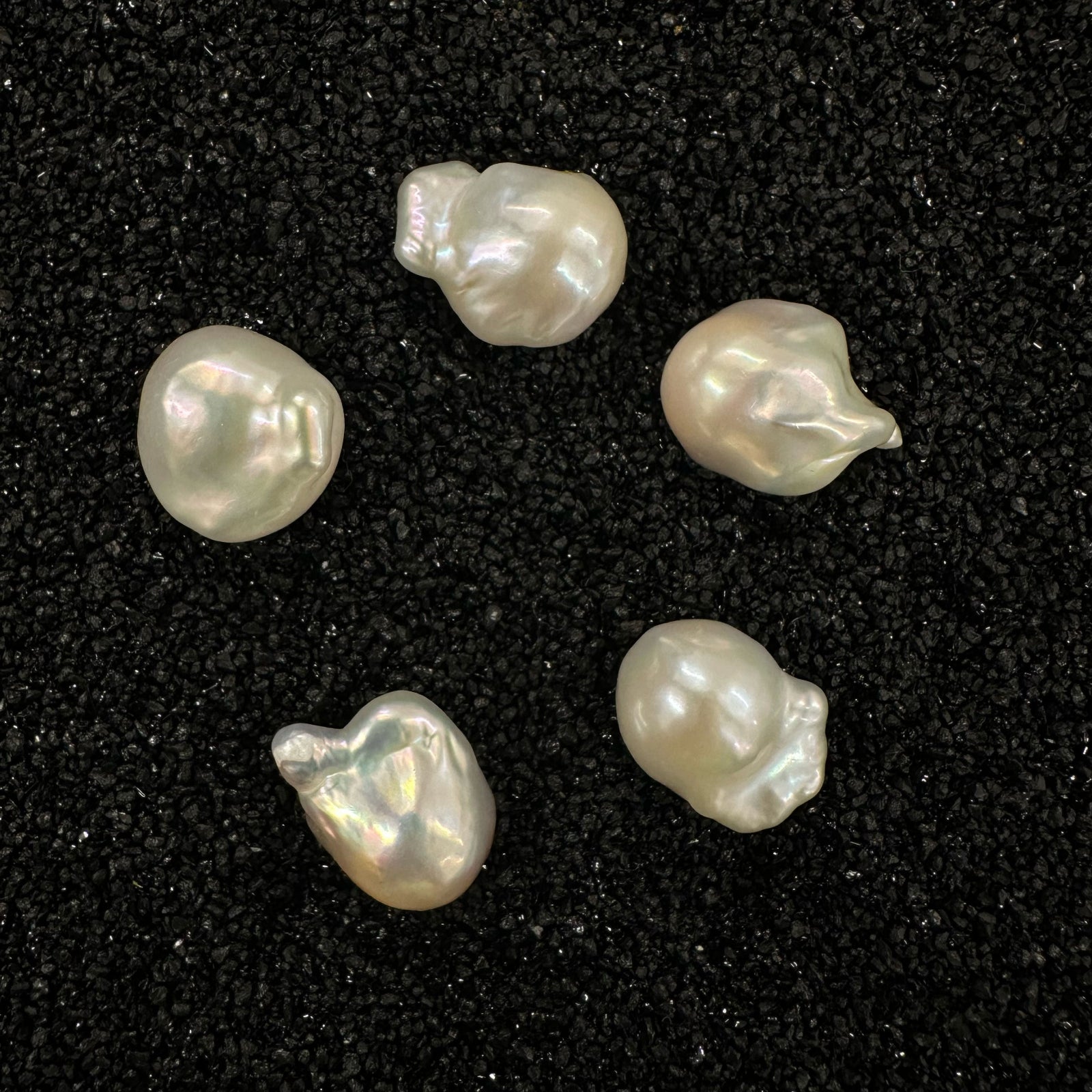 Various organically shaped baroque pearls on black sand.