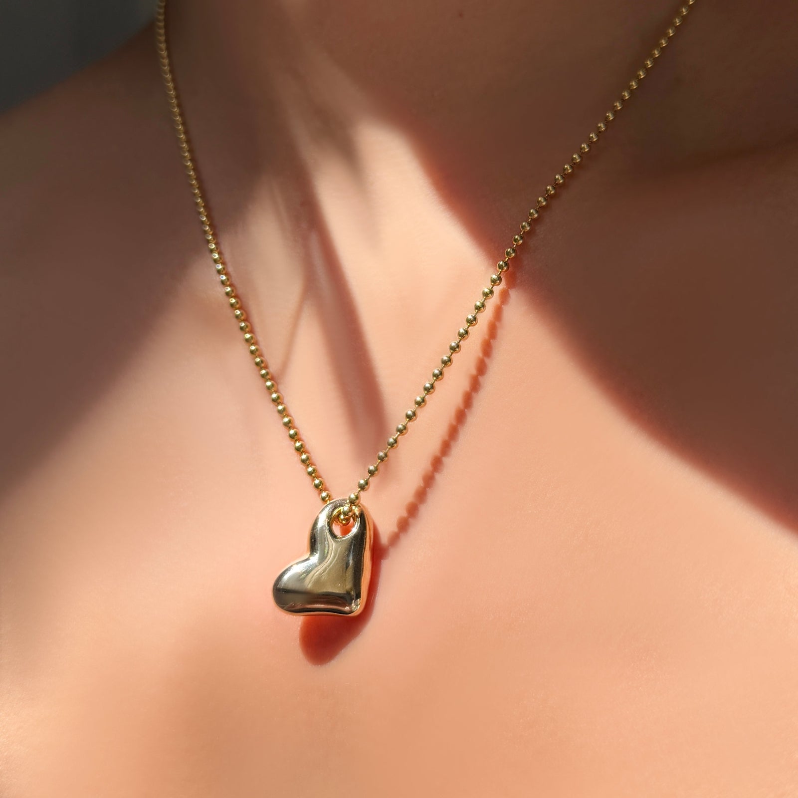 AMANDA PEARL recycled 14k gold heart charm on 2mm bead chain on a model's neck.