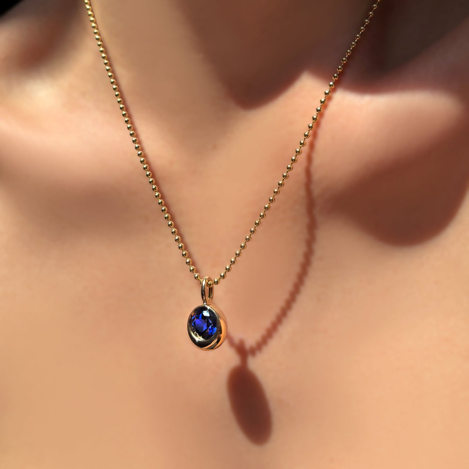 2mm bead chain in 14k yellow gold with a molten solitaire charm with round sapphire on a model's neck
