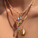 Blush sapphire necklaces layered with matching gemstone, diamond, and baroque pearl charms on a model's neck.