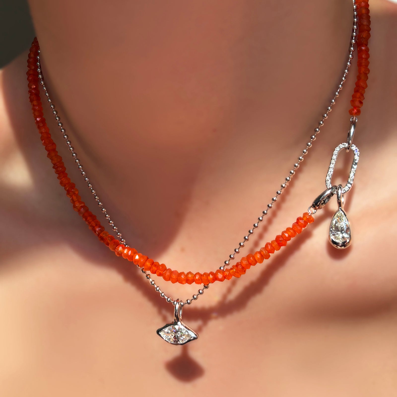 A faceted carnelian necklace with a diamond pavé face charm lock dropping a molten solitaire diamond drop charm with pear shaped diamond, layered over a white gold bead chain with molten solitaire charm with marquise diamond .