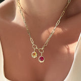 Gold chunky paperclip chain necklace with two gemstone pendants on a person wearing a beige top.