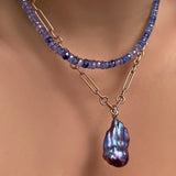 The AMANDA PEARL denim blue faceted sapphire necklace layered over an irregular cable chain necklace with Storm blue baroque pearl on 14k yellow gold ripple bale on a model's neck.