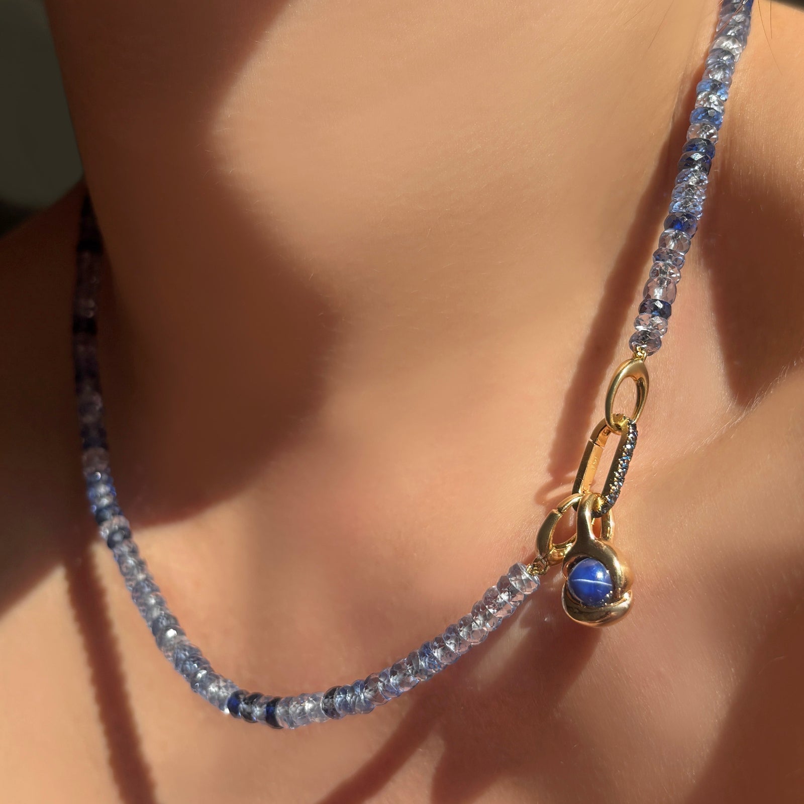 denim blue faceted sapphire necklace with sapphire charm lock and molten knot charm with star sapphire on a model's neck.