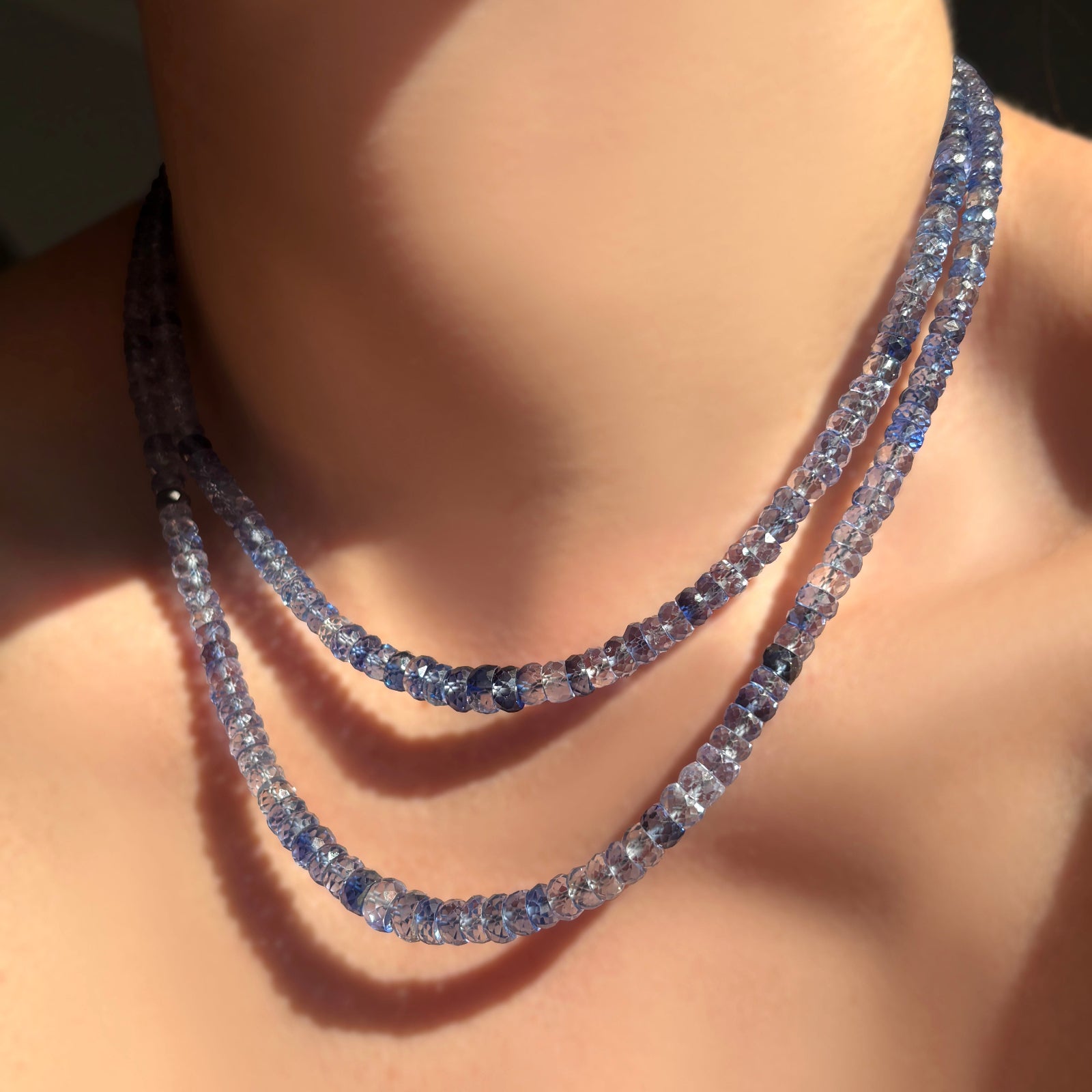 Two strands of denim blue sapphire faceted necklaces on a model's neck.