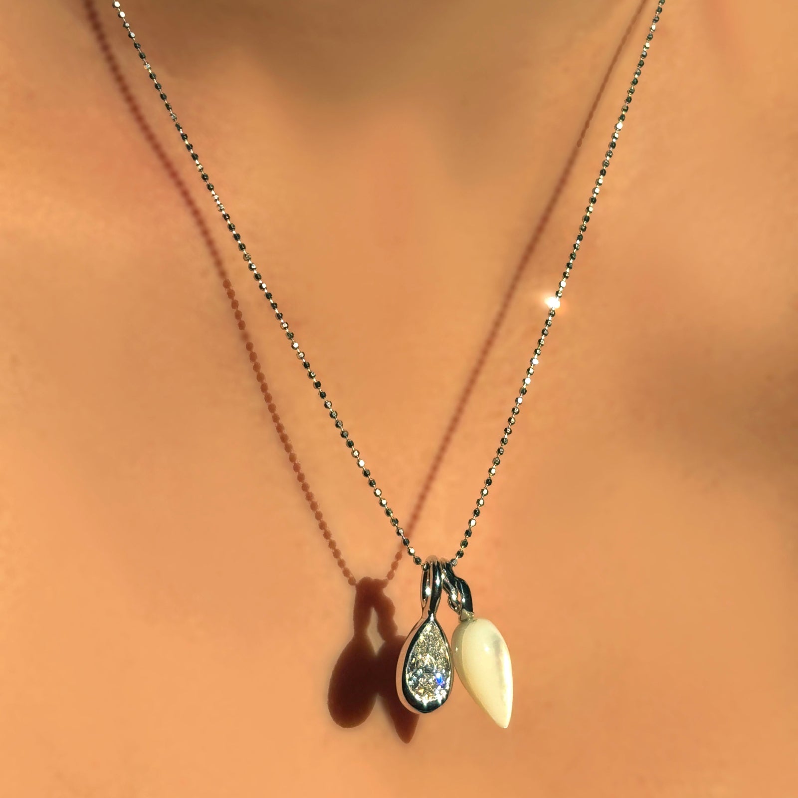 A model wears a Diamond cut bead chain in white gold, styled with the pear molten solitaire charm in white gold, and the mother of pearl drop charm in white gold.