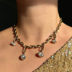 Drop link chain necklace with molten solitaire charms with marquise, round, oval diamonds hanging from small diamond charm locks on a model's neck, paired with a gold sequin top.