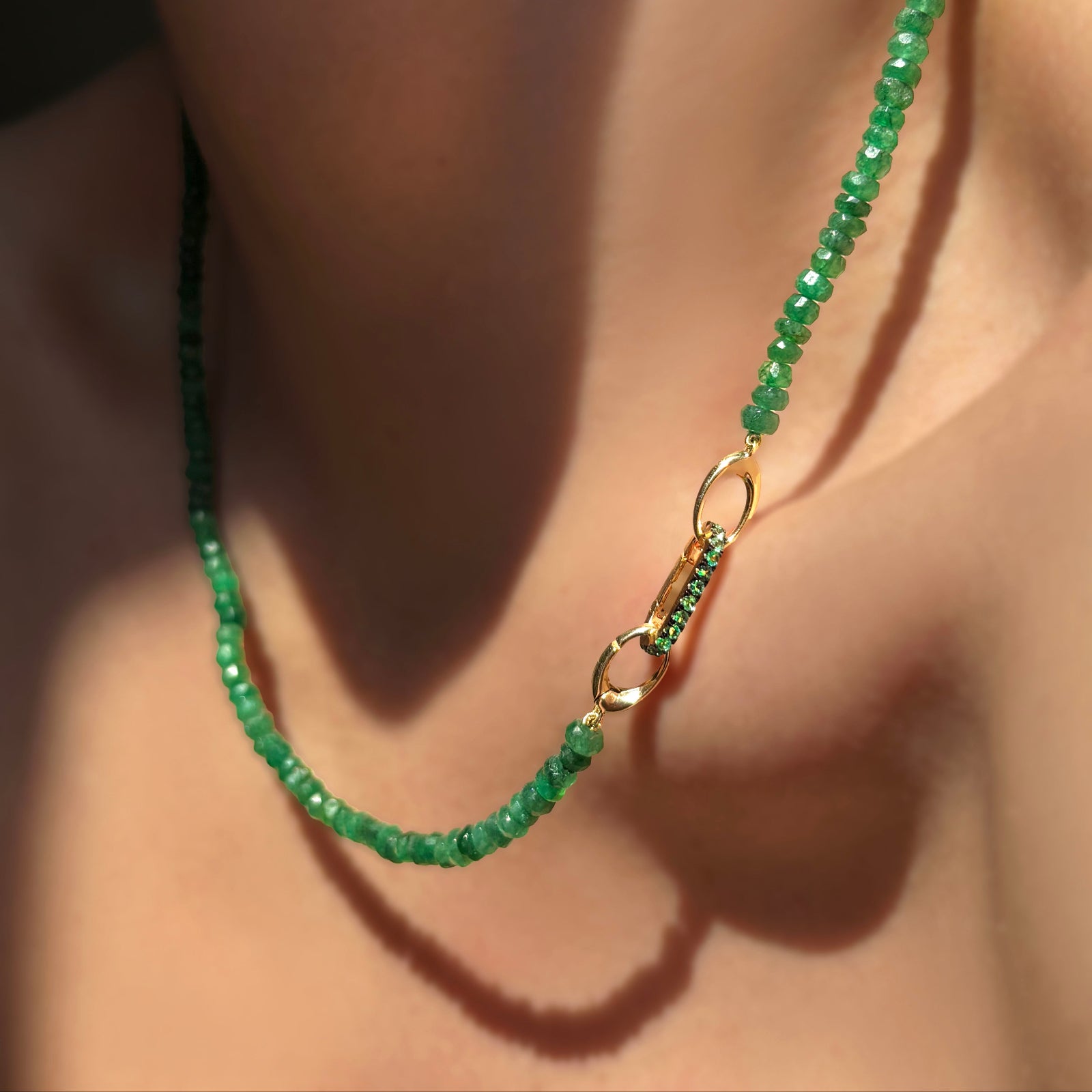 Faceted Emerald Necklace with a yellow gold evolution clasp holding a small emerald charm lock on a model's neck.