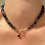 faceted rutilated quartz collar with triple link charm lock, round molten solitaire charm with ruby, and an "R" letter charm on a model's neck.