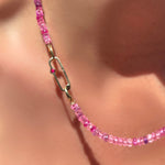 Fuchsia faceted sapphire necklace with ruby paperclip charm lock on a model's neck.