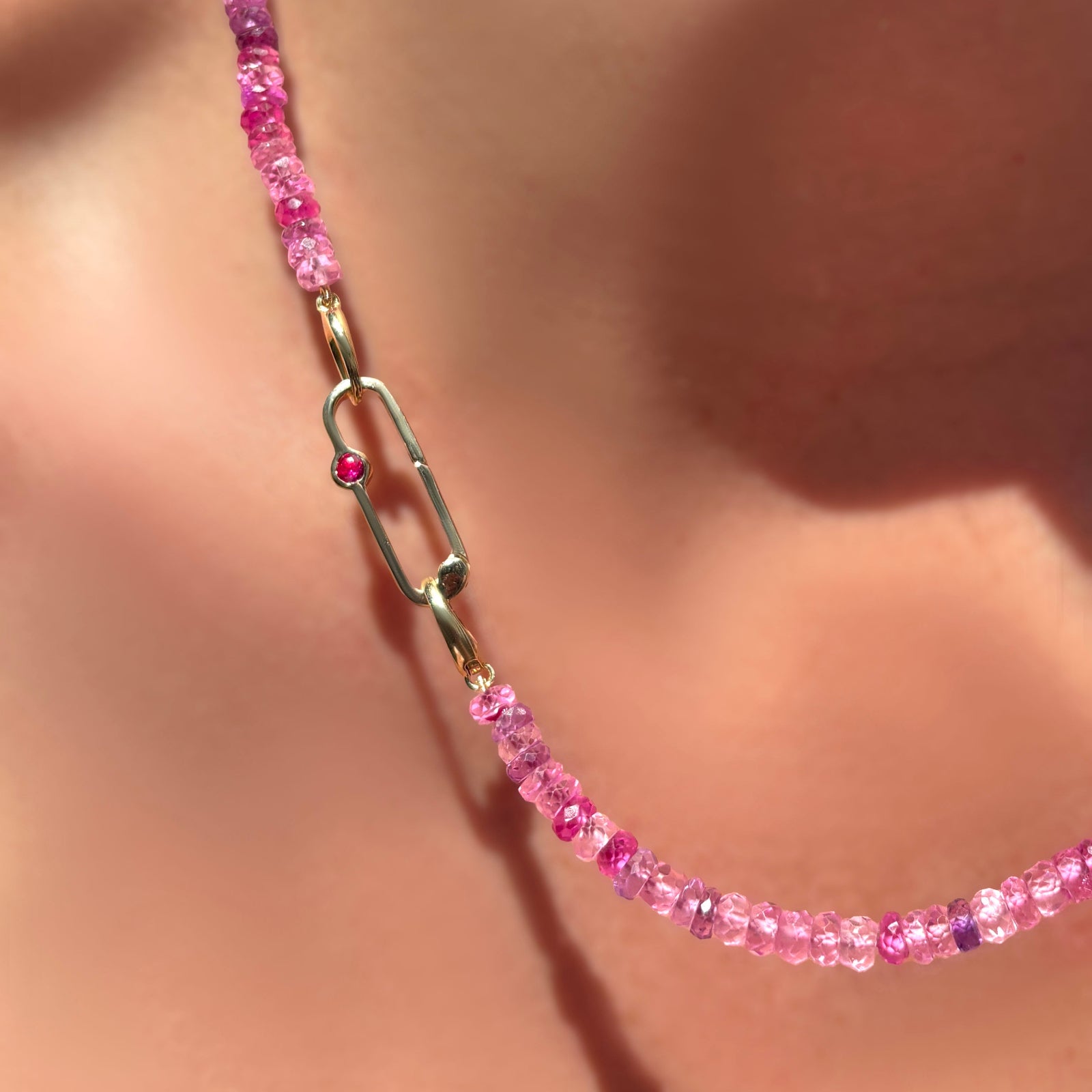 Fuchsia faceted sapphire necklace with ruby paperclip charm lock on a model's neck.