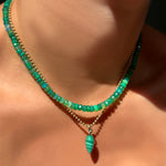 A model wears a green grass faceted opal necklace, with a 14K yellow gold bead chain, from which dangles a malachite drop charm with a 14K yellow gold ripple bail. 